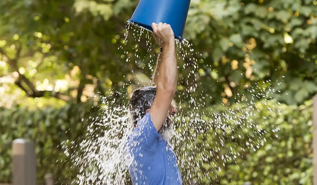 Ein Mann schüttet sich Wasser aus einem blauen Eimer über den Kopf